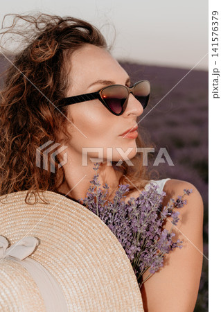 Woman lavender flower nature portrait of an elegant lady wearing a straw hat while standing in a blooming purple field 141576379