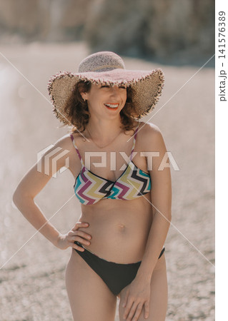 Woman summer beach, smiling woman wearing sun hat and bikini standing on sandy shore enjoying sunny vacation getaway lifestyle Woman summer beach, smiling woman wearing sun hat and bikini standing on sandy shore enjoying sunny vacation getaway lifestyle 141576389