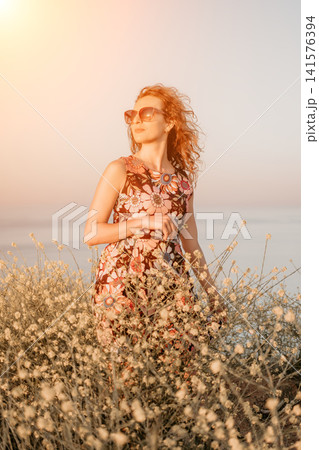 Woman flowers sunset, redheaded woman in floral dress stands among wildflowers at the beach during golden hour for summer lifestyle Woman flowers sunset, redheaded woman in floral dress stands among wildflowers at the beach during golden hour for summer lifestyle 141576394