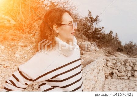 Woman Sweater Landscape Elegant woman in striped sweater and glasses gazes at a rugged landscape from a stone path. Woman Sweater Landscape Elegant woman in striped sweater and glasses gazes at a rugged landscape from a stone path. 141576425
