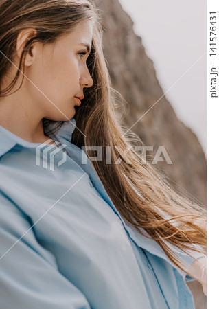 Woman portrait outdoor profile of a beautiful young lady with long hair wearing a blue shirt standing near a rock wall 141576431