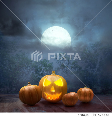 A glowing carved jack-o'-lantern and plain pumpkins under a bright full moon and cloudy sky in a dark, spooky forest during Halloween. Halloween and horror background A glowing carved jack-o'-lantern and plain pumpkins under a bright full moon and cloudy sky in a dark, spooky forest during Halloween. Halloween and horror background 141576438