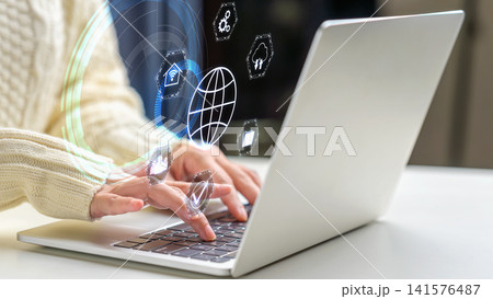 Close-up of hands typing on a laptop keyboard with abstract holographic icons representing internet connectivity, cloud computing, and digital technology. Concept of Remote working 141576487