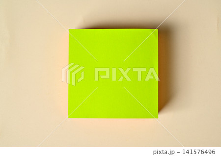 Flat lay of a blank bright green square sticky note block centered on a warm beige background with copy space 141576496