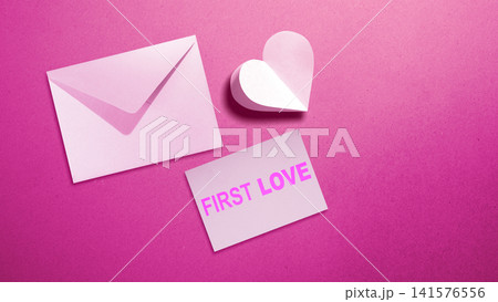 Flat lay of a pink love letter envelope, a 3D paper heart, and a card with the text 'First Love' on a textured pink background. Concept of First Love Day Flat lay of a pink love letter envelope, a 3D paper heart, and a card with the text 'First Love' on a textured pink background. Concept of First Love Day 141576556