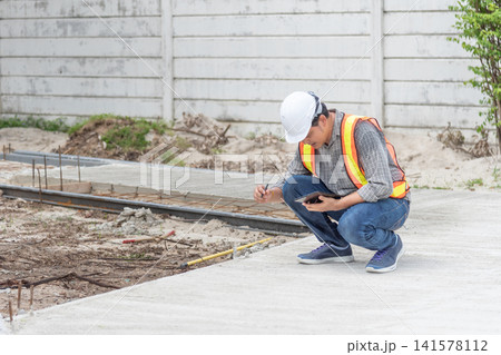 Construction engineer inspecting concrete pavement at building site using tablet taking notes while checking quality safety project progress Construction engineer inspecting concrete pavement at building site using tablet taking notes while checking quality safety project progress 141578112