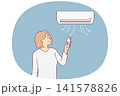 Woman stands under air conditioner and uses remote control to switch temperature mode 141578826