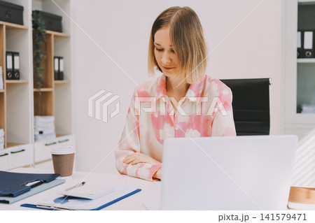 Young businesswoman smiling as she works on a laptop sitting in an modern office Young businesswoman smiling as she works on a laptop sitting in an modern office 141579471