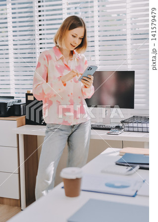 Happy beautiful Hispanic businesswoman using web service on smartphone in office workspace, working on online project on mobile phone, typing on cellphone, smiling. Banner shot 141579479