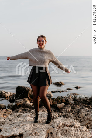 Woman Coastline Carefree young lady with arms outstretched standing on a rocky shore by the sea during golden hour 141579659
