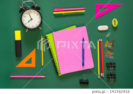 Colorful school supplies, book, and alarm clock on green. Colorful school supplies, book, and alarm clock on green. 141582916