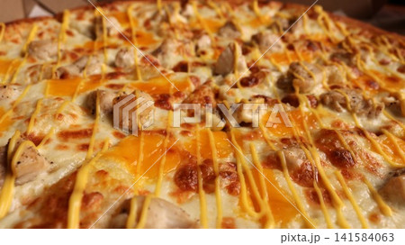 A close-up of a delicious pizza with chicken breast pieces topped with melted cheese. The dish is topped with stripes of yellow sauce, and delicious islands of cheddar are baked into the fluffy crust. 141584063