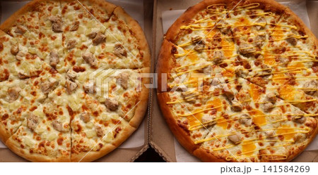 Two round pizzas in cardboard boxes. On the left is a classic Hawaiian pizza with chicken and pineapple pieces on mozzarella cheese. On the right is a cheese pizza with chicken, drizzled with sause Two round pizzas in cardboard boxes. On the left is a classic Hawaiian pizza with chicken and pineapple pieces on mozzarella cheese. On the right is a cheese pizza with chicken, drizzled with sause 141584269