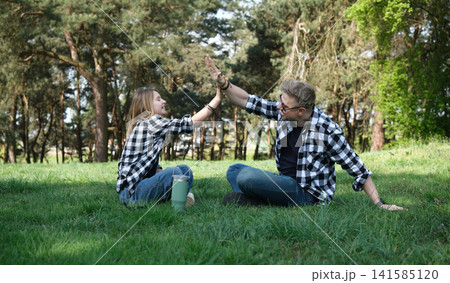 Father And Daughter Sitting On Grass In A Summer Park Giving A High Five Father And Daughter Sitting On Grass In A Summer Park Giving A High Five 141585120