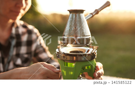 Woman Making Coffee In A Cezve On A Portable Camping Stove Boils Water Woman Making Coffee In A Cezve On A Portable Camping Stove Boils Water 141585122
