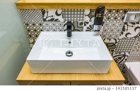 木製カウンターに置かれたモノクロ柄タイルの洗面台とスタイリッシュな黒い蛇口 木製カウンターに置かれたモノクロ柄タイルの洗面台とスタイリッシュな黒い蛇口 141585137