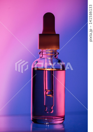Glass dropper bottle filled with colorful liquid against a gradient background of purple and blue hues, showcasing the product's clarity and design Glass dropper bottle filled with colorful liquid against a gradient background of purple and blue hues, showcasing the product's clarity and design 141586133