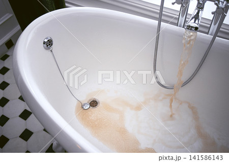 Bathtub filling with water in a modern bathroom, featuring a vintage-style faucet and a checkered floor design in black and white Bathtub filling with water in a modern bathroom, featuring a vintage-style faucet and a checkered floor design in black and white 141586143