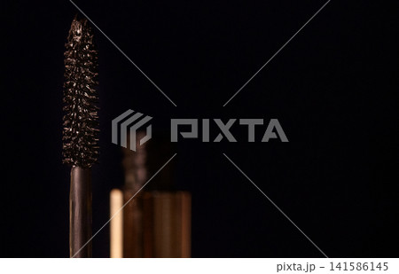 Close-up of a mascara brush with bristles, black mascara tube partially visible against a dark background, highlighting beauty and cosmetic product details Close-up of a mascara brush with bristles, black mascara tube partially visible against a dark background, highlighting beauty and cosmetic product details 141586145