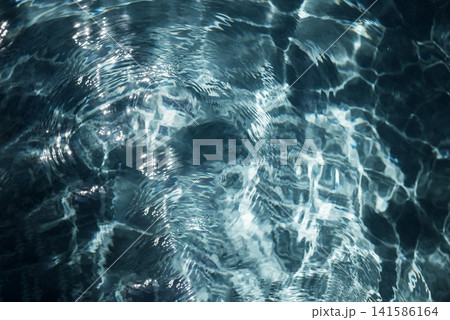 Clear blue water surface with ripples and reflections, showcasing light patterns and textures in a tranquil aquatic environment Clear blue water surface with ripples and reflections, showcasing light patterns and textures in a tranquil aquatic environment 141586164