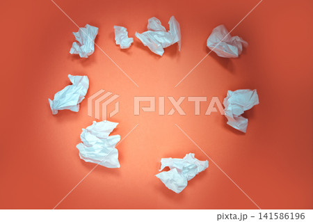 Crumpled white paper balls arranged in a circular pattern on a vibrant orange background, showcasing creative waste and artistic expression in minimalistic design 141586196