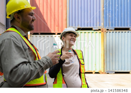 Happy pregnant female engineer and male colleague taking refreshing water break and talking together at shipping cargo container terminal Happy pregnant female engineer and male colleague taking refreshing water break and talking together at shipping cargo container terminal 141586348