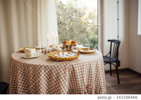 Cozy dining table set with checkered tablecloth, featuring delicious baked goods, fresh apples, and candles, creating a warm and inviting atmosphere for gatherings Cozy dining table set with checkered tablecloth, featuring delicious baked goods, fresh apples, and candles, creating a warm and inviting atmosphere for gatherings 141586466