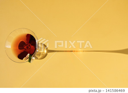 Close-up of a martini glass on a yellow background. View from above. An elegant goblet with a red alcoholic sparkling drink decorated with lime zest. Sunlight. Close-up of a martini glass on a yellow background. View from above. An elegant goblet with a red alcoholic sparkling drink decorated with lime zest. Sunlight. 141586469