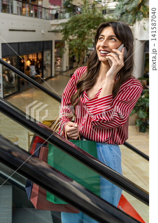 Pretty young woman standing on the escalator and talking on the phone 141587040