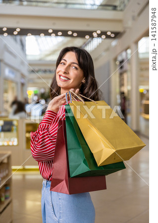 Smiling young woman feeling happy and contented while doing shopping in a shopping center Smiling young woman feeling happy and contented while doing shopping in a shopping center 141587948