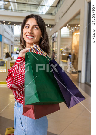 Dark-haired cute young woman smiling nicely after a successful shopping Dark-haired cute young woman smiling nicely after a successful shopping 141587957