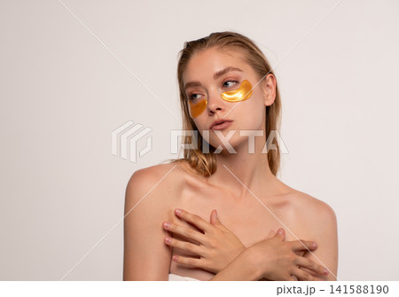 Woman wearing under eye patches, applying anti-aging facial product for skin treatment and beauty routine 141588190