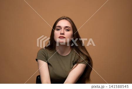 Young brunette woman looking at camera with serious and confident expression against a brown background Young brunette woman looking at camera with serious and confident expression against a brown background 141588545