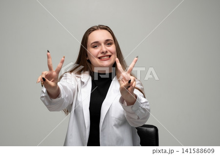 Young woman smiling and showing victory hand signs, expressing happiness, success, and positive attitude Young woman smiling and showing victory hand signs, expressing happiness, success, and positive attitude 141588609