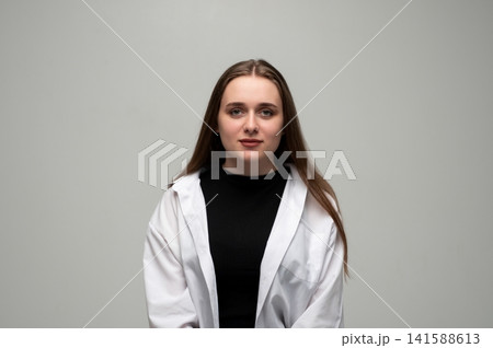 Young woman with brown hair wearing a white shirt and black top, standing confidently looking at the camera 141588613