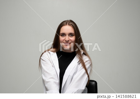 Young woman sits comfortably, with a pleasant smile and a natural beauty, set against a simple background Young woman sits comfortably, with a pleasant smile and a natural beauty, set against a simple background 141588621