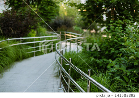 Curving landscaped pedestrian pathway with ornamental grasses and lush greenery showcasing contemporary urban landscape and sustainable item. Curving landscaped pedestrian pathway with ornamental grasses and lush greenery showcasing contemporary urban landscape and sustainable item. 141588892