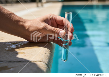 Hand holding test tube with blue liquid near swimming pool edge 141589050
