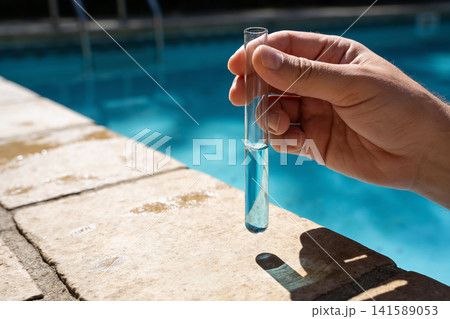 Hand holding test tube with blue liquid near swimming pool edge 141589053