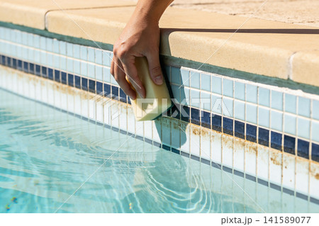 Hand cleaning pool tiles with a sponge to remove waterline stains Hand cleaning pool tiles with a sponge to remove waterline stains 141589077
