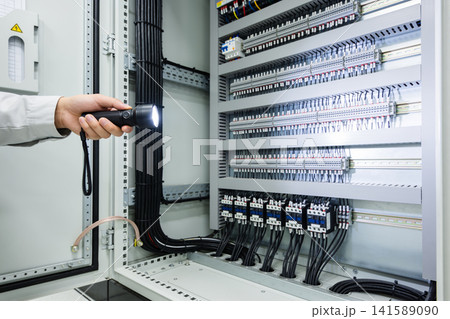 Electrician inspecting a complex electrical panel with a flashlight 141589090