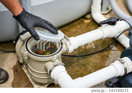 Gloved hand opening pool pump basket to remove debris and fallen leaves Gloved hand opening pool pump basket to remove debris and fallen leaves 141589231