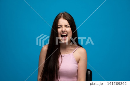Young woman expressing strong anger, screaming frustration and feeling stressed against a blue background Young woman expressing strong anger, screaming frustration and feeling stressed against a blue background 141589262