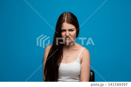 Young woman making a disgusted facial expression on blue background, showing aversion or dislike Young woman making a disgusted facial expression on blue background, showing aversion or dislike 141589397