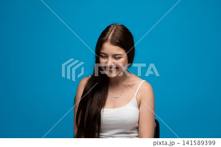 Young woman smiling and looking down, feeling happy and cheerful with natural beauty on blue background Young woman smiling and looking down, feeling happy and cheerful with natural beauty on blue background 141589399