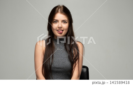 Young woman making a playful funny face sticking out tongue looking at camera in a studio portrait 141589418