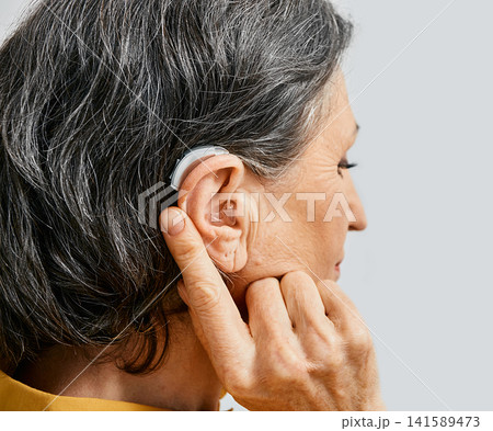 Hearing aid behind the ear of senior woman, close-up Hearing aid behind the ear of senior woman, close-up 141589473