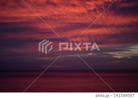 Dramatic red sunset over dark sea with textured clouds in sky 141589507