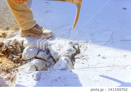 Worker uses pickaxe to break concrete at construction site dust rises from ground. Worker uses pickaxe to break concrete at construction site dust rises from ground. 141589702