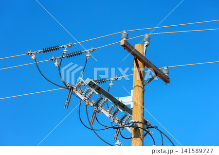 Power lines are seen on wooden pole with clear blue sky background Power lines are seen on wooden pole with clear blue sky background 141589727